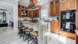 A modern kitchen with wooden cabinets, a marble island, and a black oven. - Oak & Ocean * Pet Friendly, Boat Launch, Firepit, Hot Tub, Grill (Santa Rosa Beach)