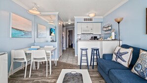 A compact living space with a dining area, kitchen, and a blue sofa with starfish pillows. - Salt Therapy, Great Amenities, Pool, Walk To Beach! (Galveston)