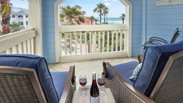 A balcony with wicker furniture, two wine glasses, and a bottle of wine. - Sea N Palms located at the award-winning Dawn Condominiums- 'Best of Galveston 2024' (Galveston)