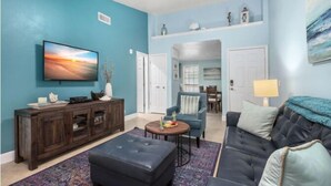 A living room with a TV, dark wood entertainment center, a blue sofa, and a patterned rug. - Sea N Palms located at the award-winning Dawn Condominiums- 'Best of Galveston 2024' (Galveston)