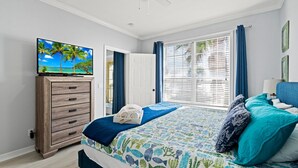 A bedroom with a bed, a TV on a wooden cabinet, a window with curtains, and a door. - Ocean View Condo w/ resort amenities! (Galveston)