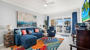 A living room with a blue sectional sofa, a colorful rug, and a large painting on the wall. - Ocean View Condo w/ resort amenities! (Galveston)