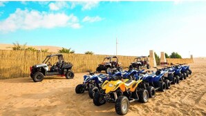 Une rangée de quads est stationnée sur une surface sablonneuse, avec une clôture en bois et un ciel dégagé en arrière-plan.