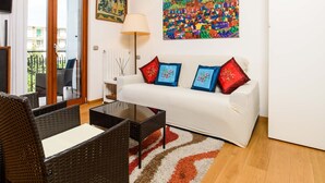 Een woonkamer met een bank, twee fauteuils, een salontafel, een schilderij en een plafondventilator.