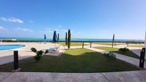 Zona de piscina amb gandules i ombrel·les, un jardí ben cuidat i vista a l'oceà.