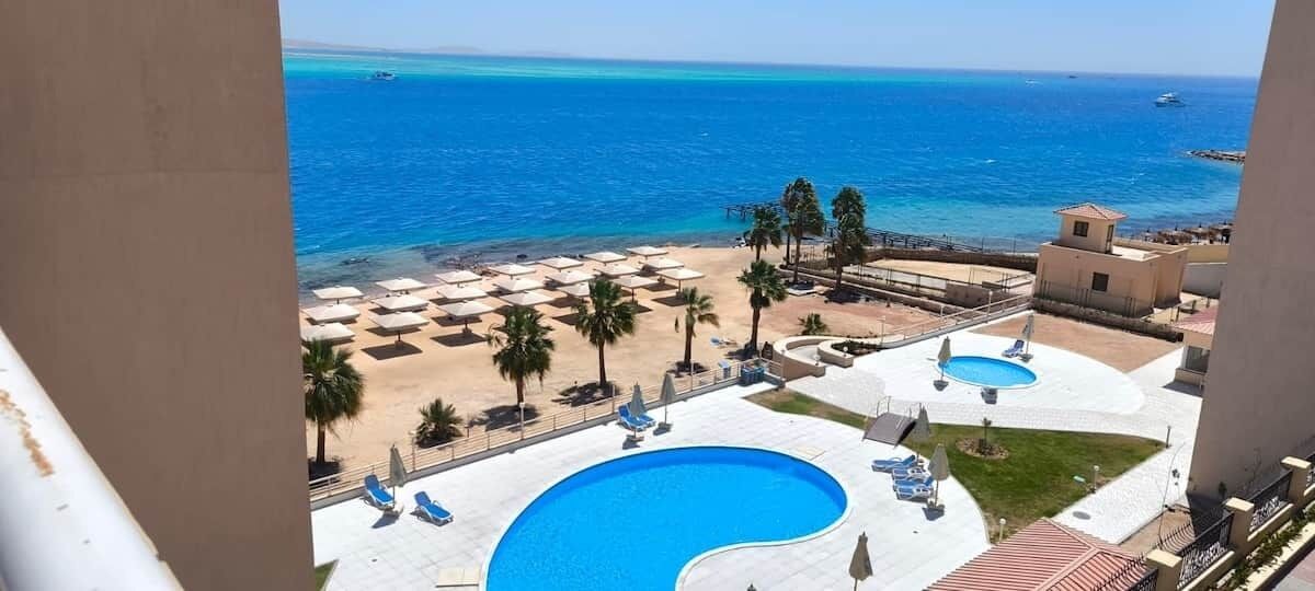 A resort with a pool area, beach umbrellas, and a view of the sea.
