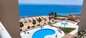 A resort with a pool area, beach umbrellas, and a view of the sea.