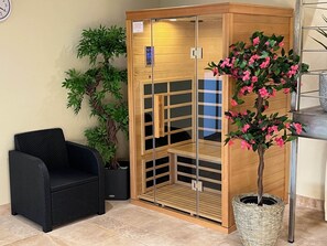 A sauna room with a wooden door, a black chair, and a potted plant with pink flowers. - My little paradise / private indoor pool (Lournand)