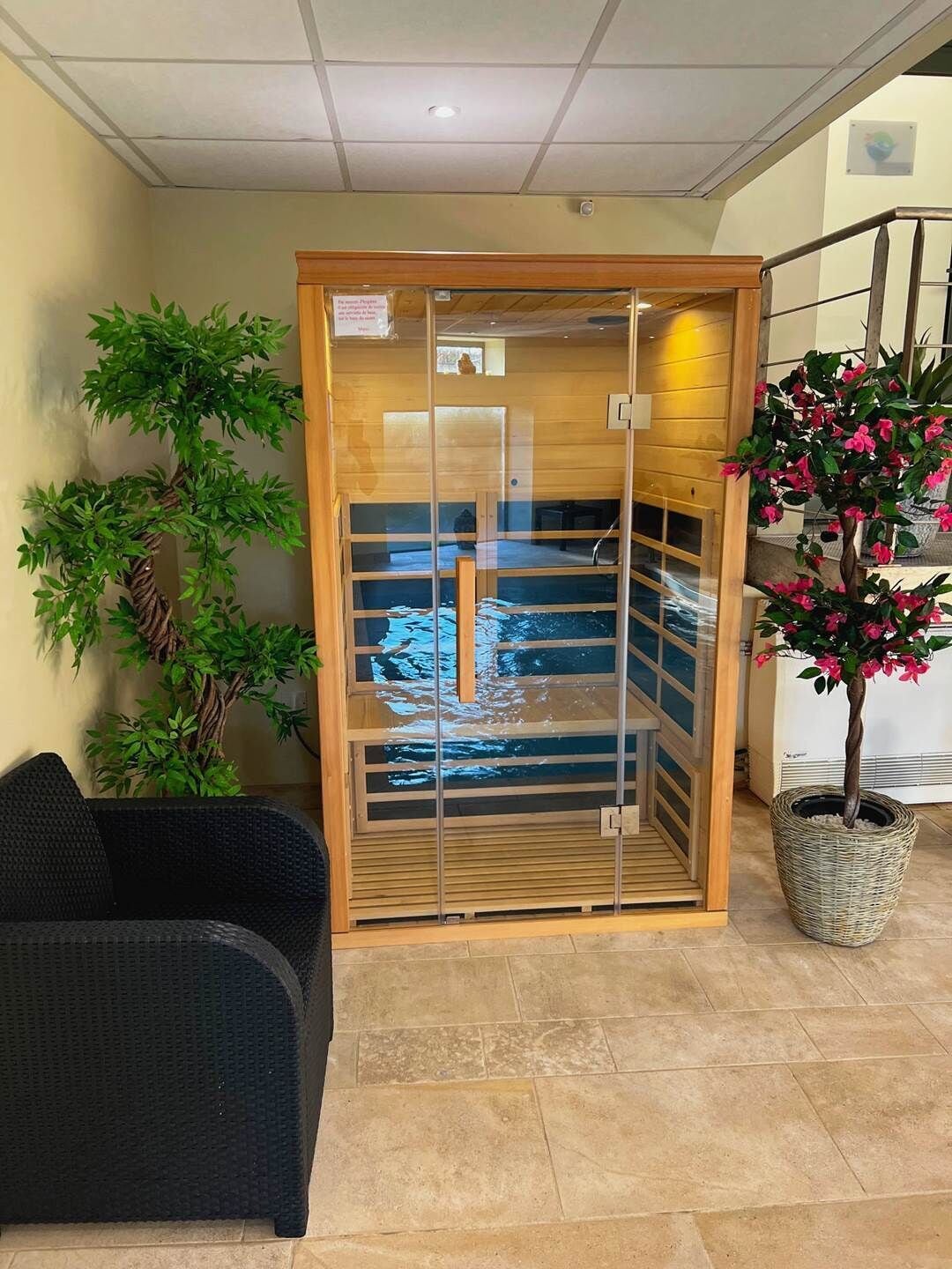 Un cuarto de spa con una puerta de madera, una silla de mimbre negro y una planta en maceta con flores rosadas.