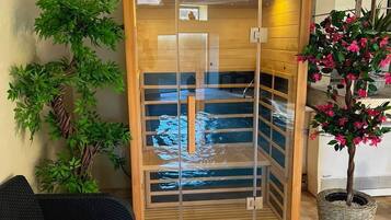 Un cuarto de spa con una puerta de madera, una silla de mimbre negro y una planta en maceta con flores rosadas.
