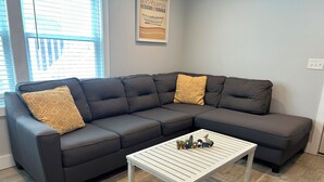 A modern living room with a dark gray sectional sofa, two patterned pillows, and a white coffee table with decorative items.