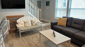 A living room with a sofa, a chair, a coffee table, a TV, and a staircase.