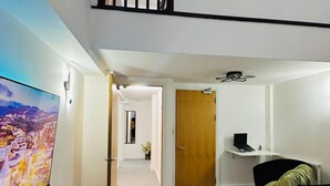A modern living room with a flat-screen TV, a sofa, a coffee table, and a small desk with a laptop. - Home Away From Home- City Centre Gem (Derby)