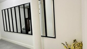 A hallway with a white column, a black-framed mirror, and a vase with flowers. - Home Away From Home- City Centre Gem (Derby)
