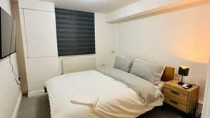 A bedroom with a bed, bedside table, lamp, and a window with blinds. - Home Away From Home- City Centre Gem (Derby)