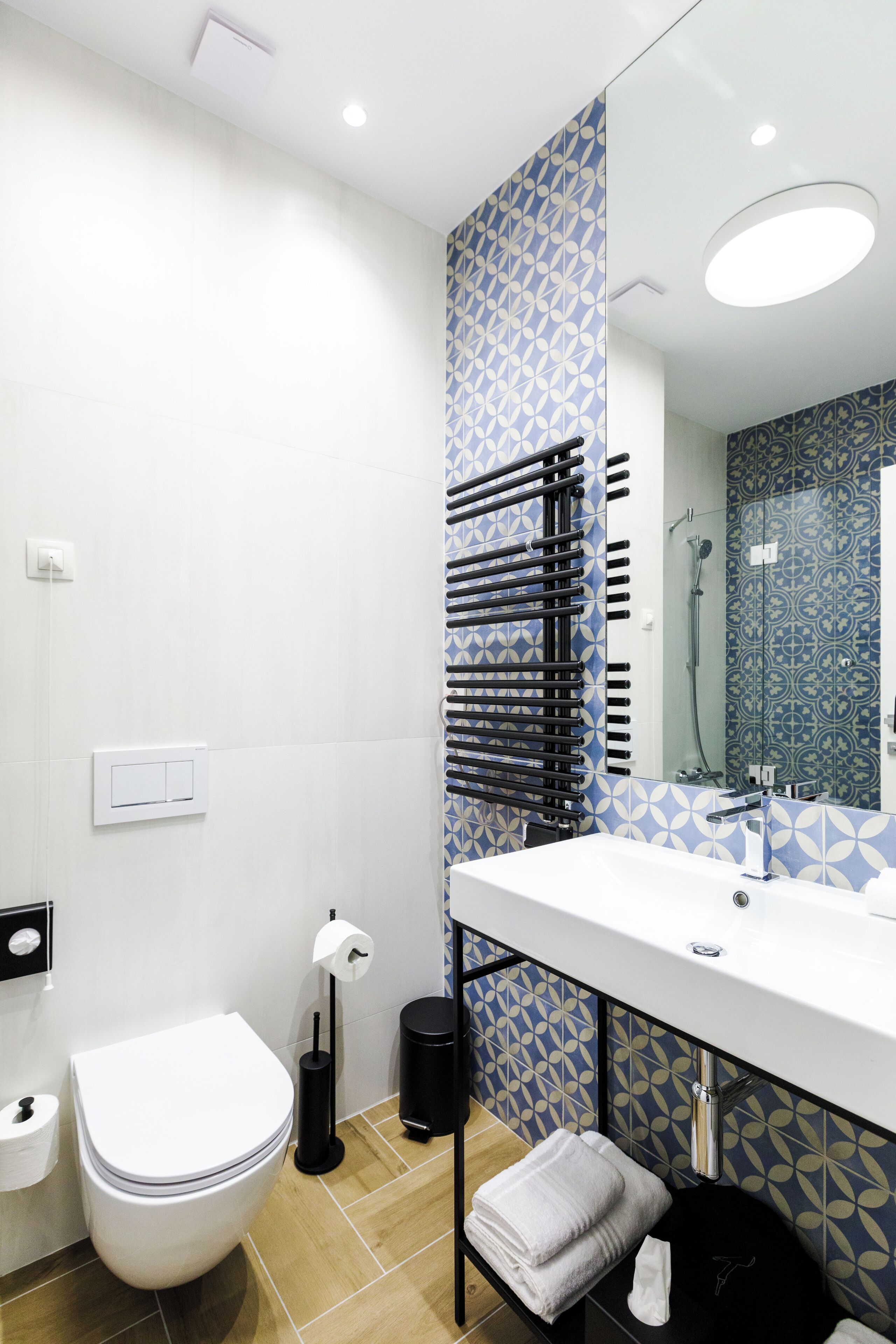 Um banheiro moderno com vaso sanitário branco, pia com espelho e azulejos estampados.