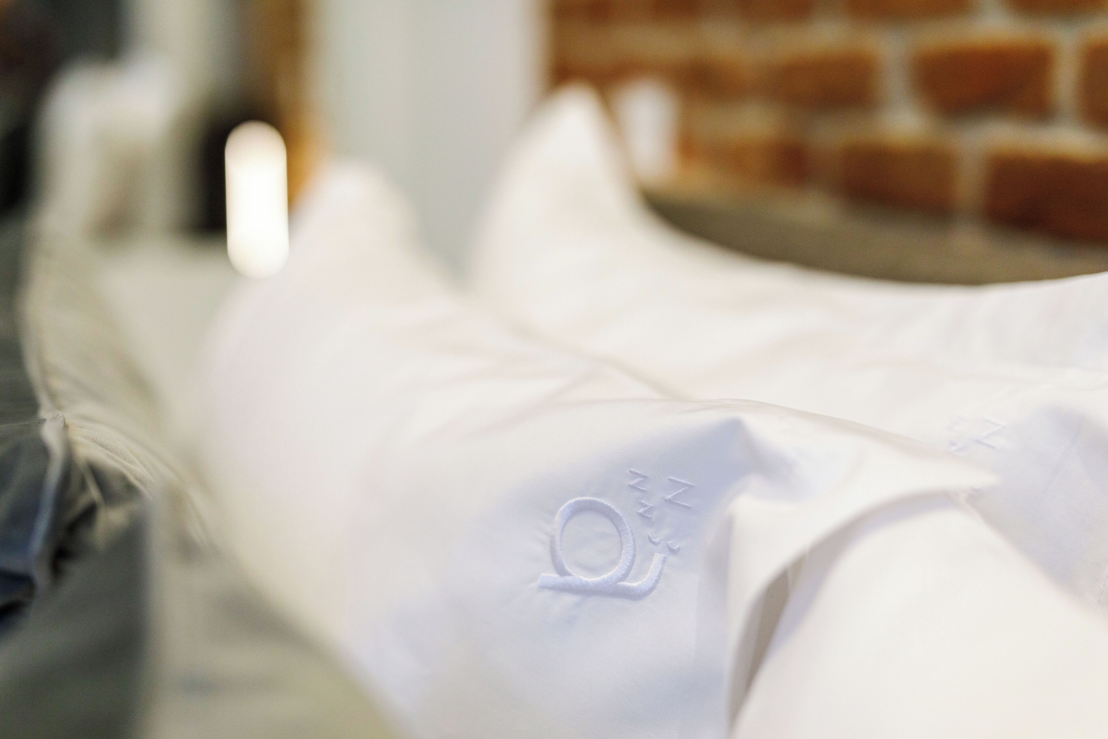 A close-up of a white pillow with an embroidered logo.
