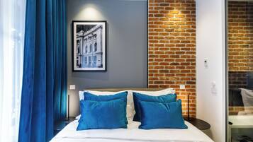 Quarto de hotel moderno com uma cama grande, almofadas azuis, um quadro na parede e uma parede de tijolos decorativa.