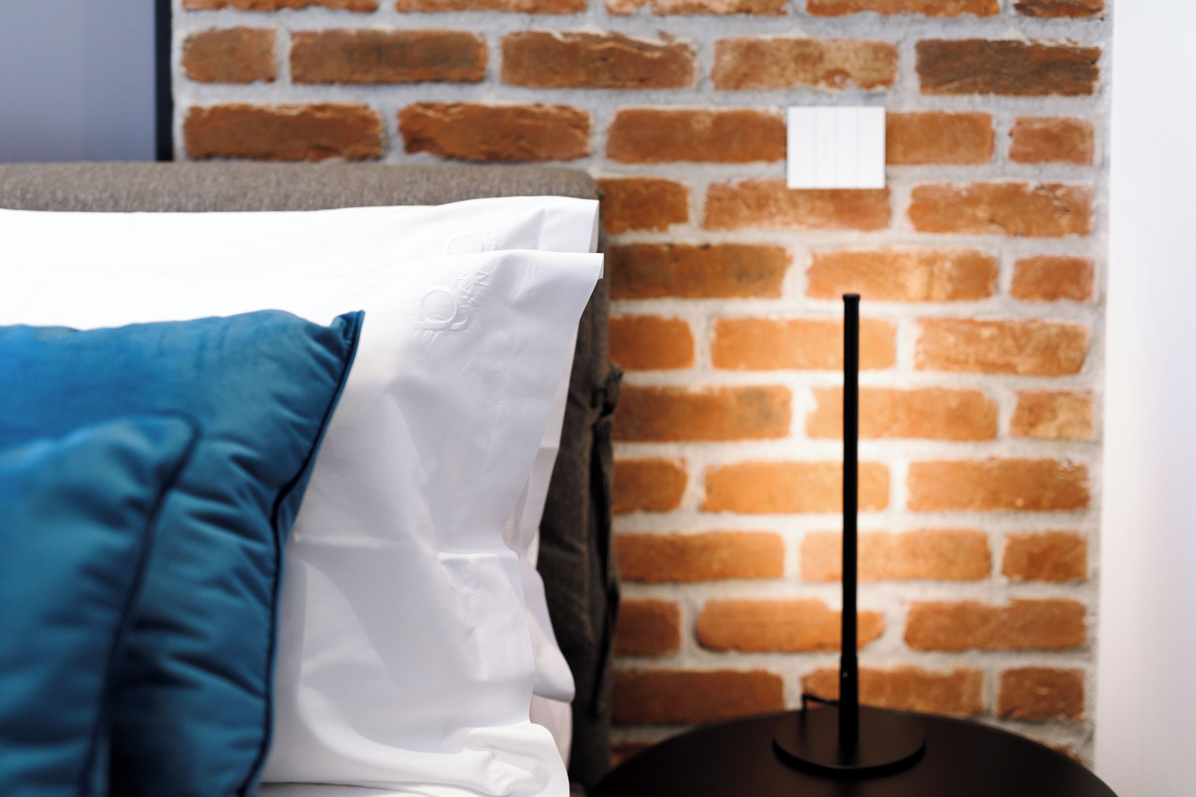 A bed with white and blue bedding against a brick wall.