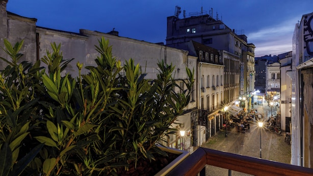 A balcony with a view of a cobblestone street at dusk, overlooking a building with a sign that reads "Mansion Hotel." - OLD TOWN SNAIL Design Apartments (Bucharest)