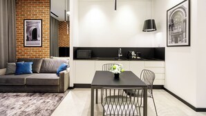 A modern living space with a sofa, a dining table with chairs, a kitchen area, and a brick wall with a framed picture. - OLD TOWN SNAIL Design Apartments (Bucharest)