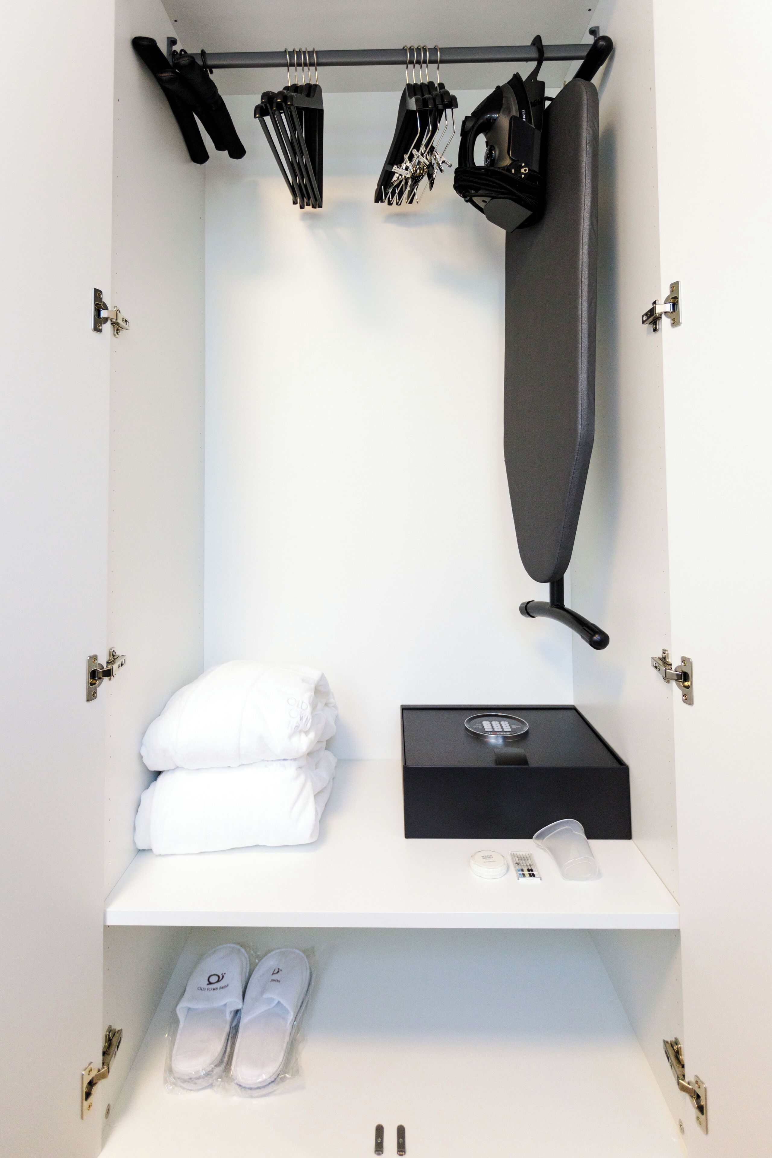 Un placard bien rangé, avec des vêtements suspendus, une paire de chaussures et une boîte noire posée sur une étagère.