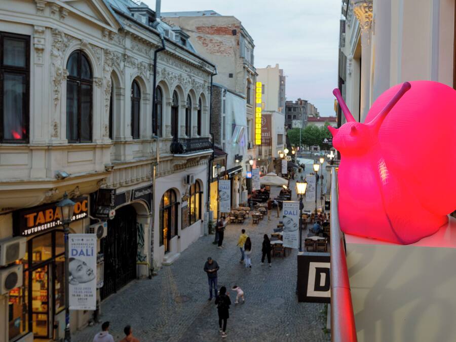 A cobblestone street with historic buildings, outdoor seating, and a large illuminated sculpture.