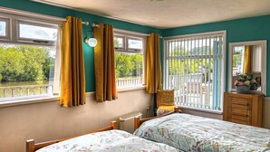 A bedroom with two beds, a window with curtains, a chair, a dresser, and a view of greenery outside. - 2 bedroom accommodation in Shrawley, near Worcester (Shrawley, near Worcester)