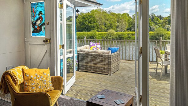 A room with a yellow armchair, a wicker sofa, and a small wooden table. There is a glass door leading to an outdoor deck with a wicker sofa and a chair. - 2 bedroom accommodation in Shrawley, near Worcester (Shrawley, near Worcester)