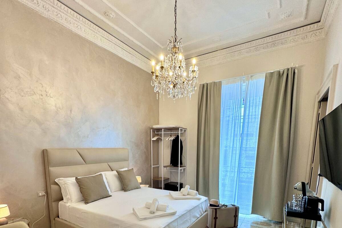 Una habitación de hotel con una cama grande, un candelabro, un televisor y un escritorio con una cesta.