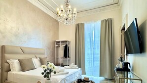 A hotel room with a large bed, a chandelier, a TV, and a breakfast trolley. - Home To Salerno B&B (Salerno)