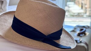 A straw hat with a dark ribbon placed on a white surface, likely a bed or couch, in a room with a view of buildings through a window. - Home To Salerno B&B (Salerno)