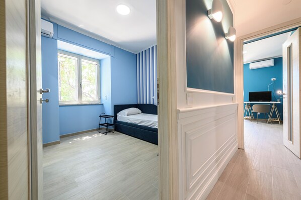 A room with a bed, a window, a desk with a chair, and an air conditioning unit.