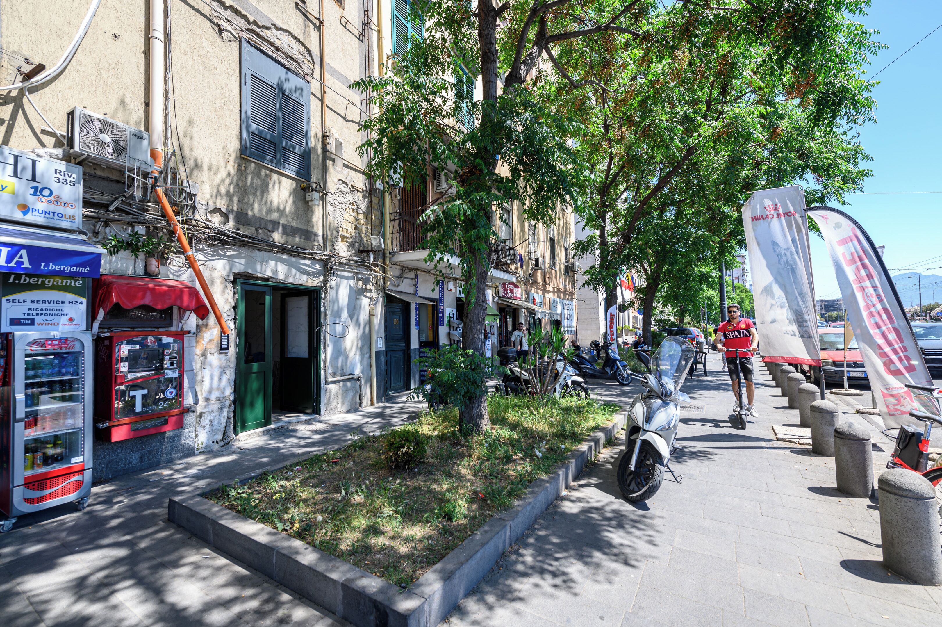 A narrow street lined with buildings, vending machines, and a tree.