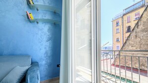 Une pièce avec un mur bleu, un canapé gris et une porte-fenêtre coulissante donnant sur un balcon extérieur.