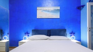 Une chambre à coucher avec un lit, du linge de lit blanc, un tableau représentant une scène de plage et des lampes de chevet en forme d’étoile.