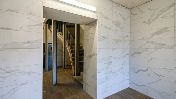 Un couloir aux murs de marbre et au plancher en bois, qui mène à un escalier.