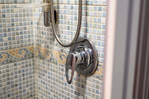 A shower with a chrome faucet and a flexible hose, set against a tiled wall with a mosaic pattern.