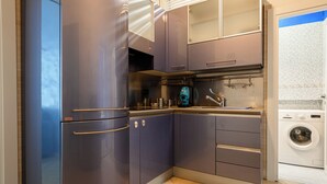 Une cuisine compacte avec des meubles de couleur sombre, un four à micro-ondes encastré et un lave-linge dans la pièce adjacente.