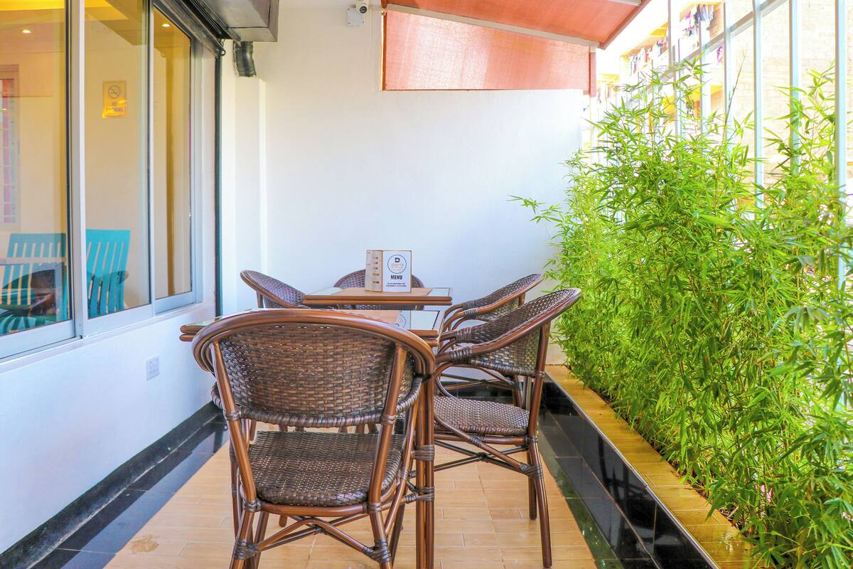 A terrace with wicker chairs and a table, a menu stand, and a bamboo plant wall.