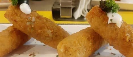 A plate of breaded and fried food items, garnished with a white sauce and herbs, on a white rectangular plate.