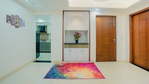 A hallway with a colorful rug, a wooden door, and a cabinet with a plant. - Lime Tree Hotel Golf Course Extension Rd (Gurugram)