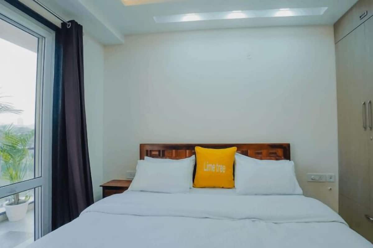 A hotel room with a bed, a nightstand, a wardrobe, and a window with a view of palm trees.