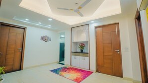 A modern room with a ceiling fan, wooden doors, a kitchen area, and a colorful rug. - Lime Tree Hotel Golf Course Extension Rd (Gurugram)