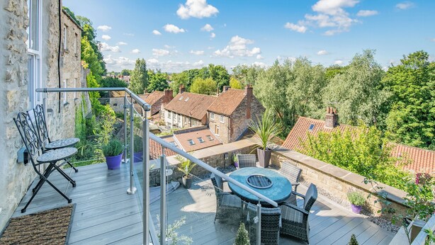 A wooden deck with outdoor furniture, a glass balustrade, and a view of surrounding buildings and greenery. - 3 bedroom accommodation in Pickering (Pickering)