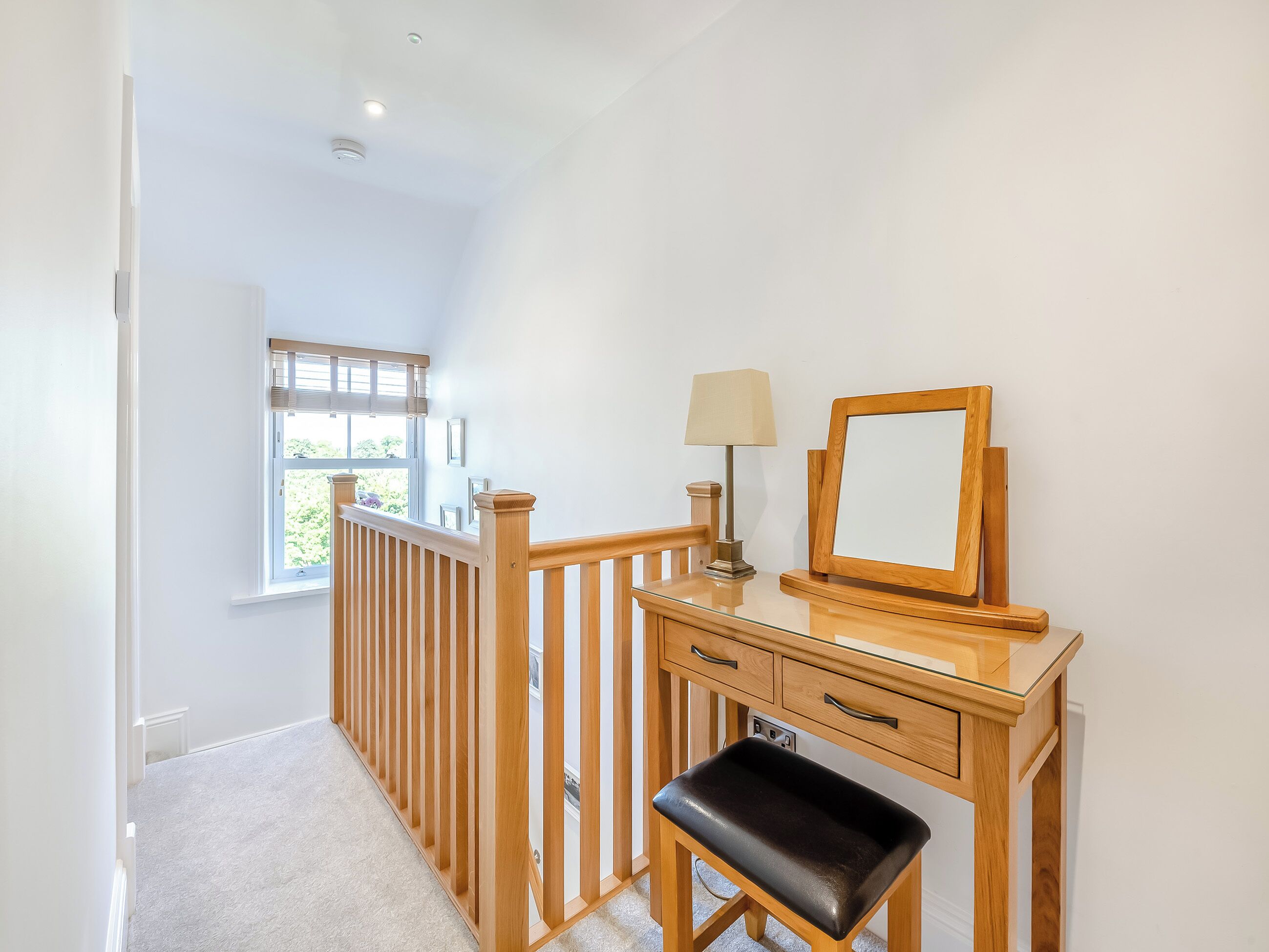 A hallway with a wooden bench, a desk with a lamp, and a mirror.