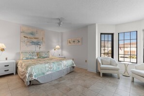 A bedroom with a bed, two bedside tables, a ceiling fan, a chair, a small table, and a window with blinds. - 3 Bdrm @ Sea Marsh II-Pool- Corner Oceanfront View (North Myrtle Beach)