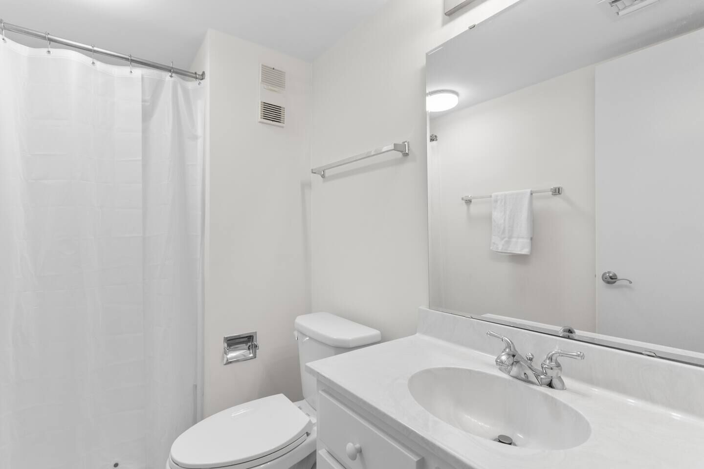 A bathroom with a shower curtain, toilet, sink, and a mirror.