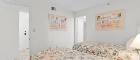 Un dormitorio con dos camas, paredes blancas y dos cuadros enmarcados.