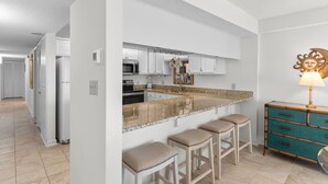 Una cocina moderna con armarios blancos, encimera de granito y una isla integrada con taburetes de bar.